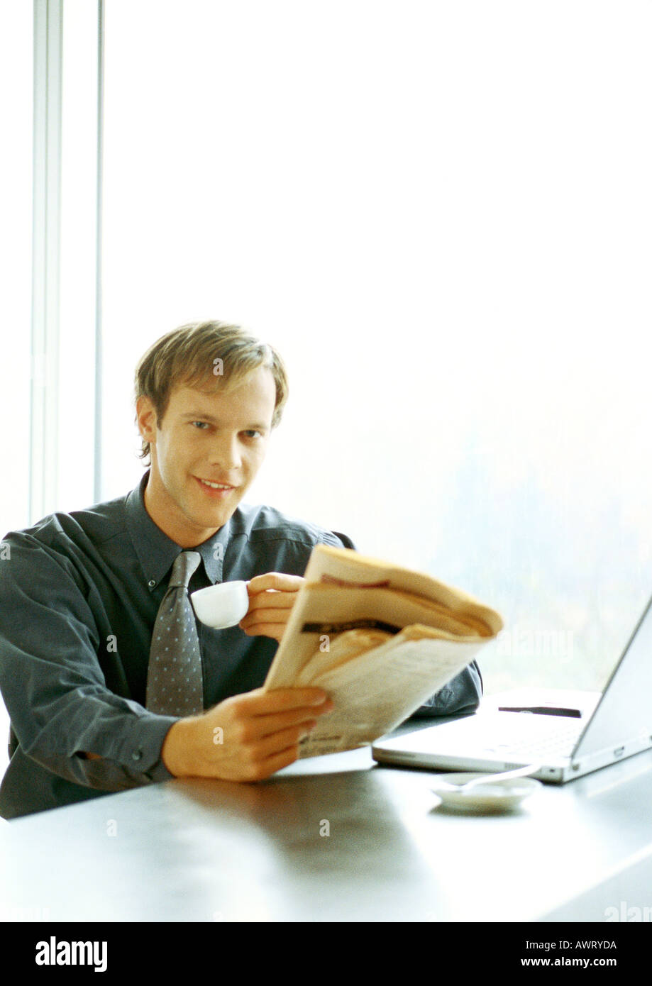 Businessman sitting at desk, de boire et de la lecture Banque D'Images