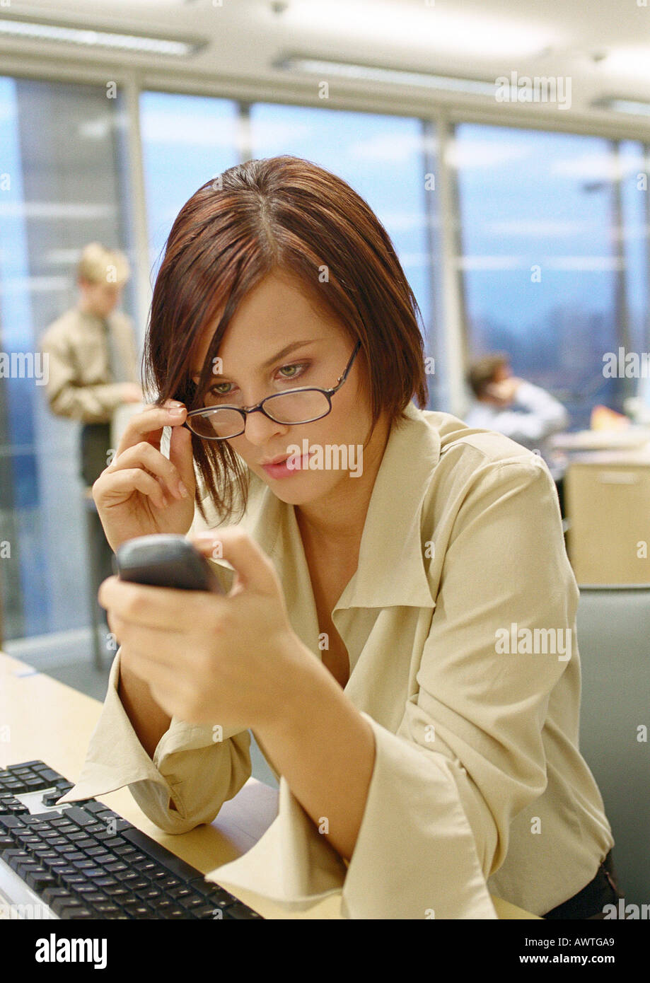 Businesswoman adjusting glasses looking at phone, dans le bureau, Close up. Banque D'Images
