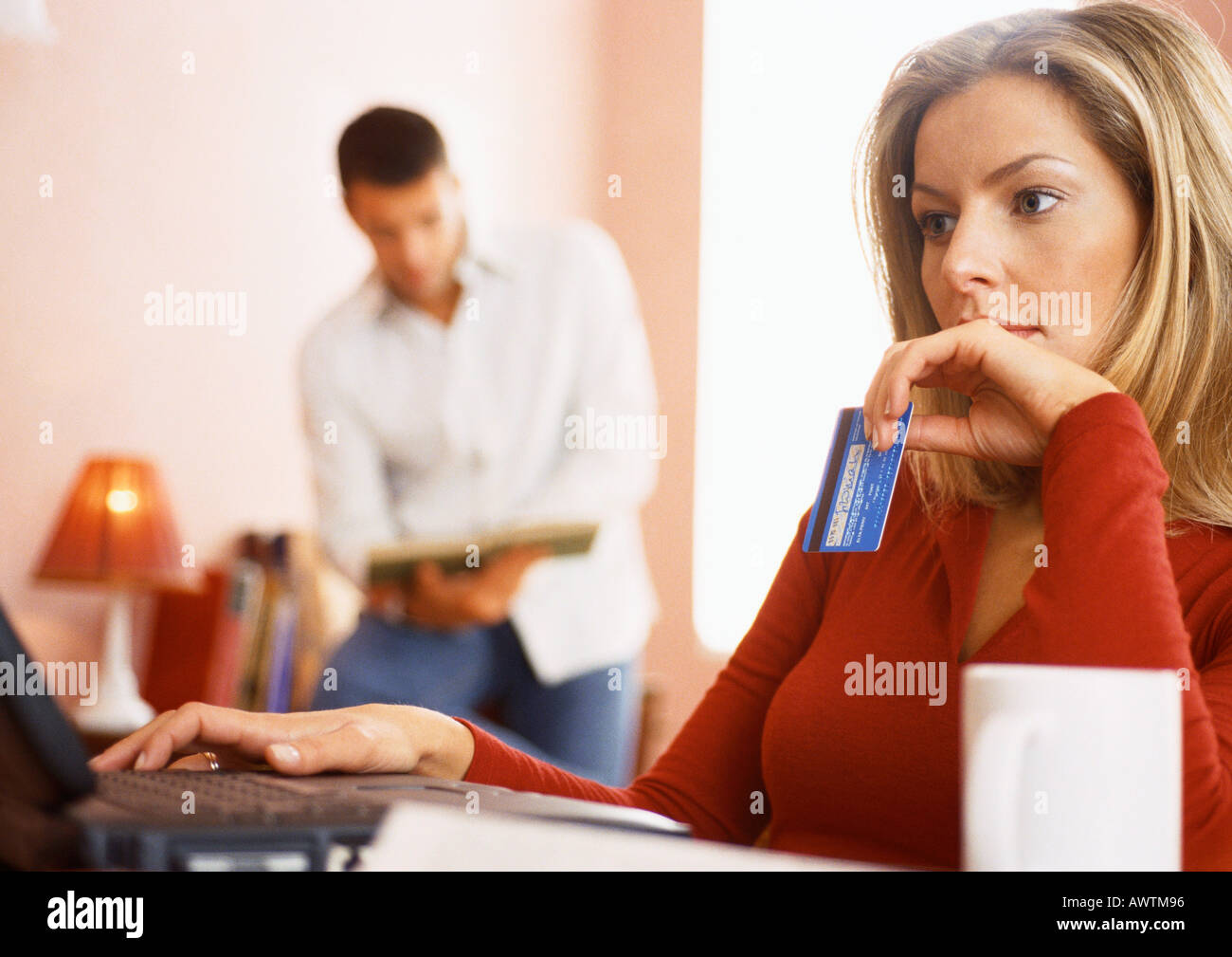 Woman using computer and holding credit card, l'homme la lecture en arrière-plan. Banque D'Images