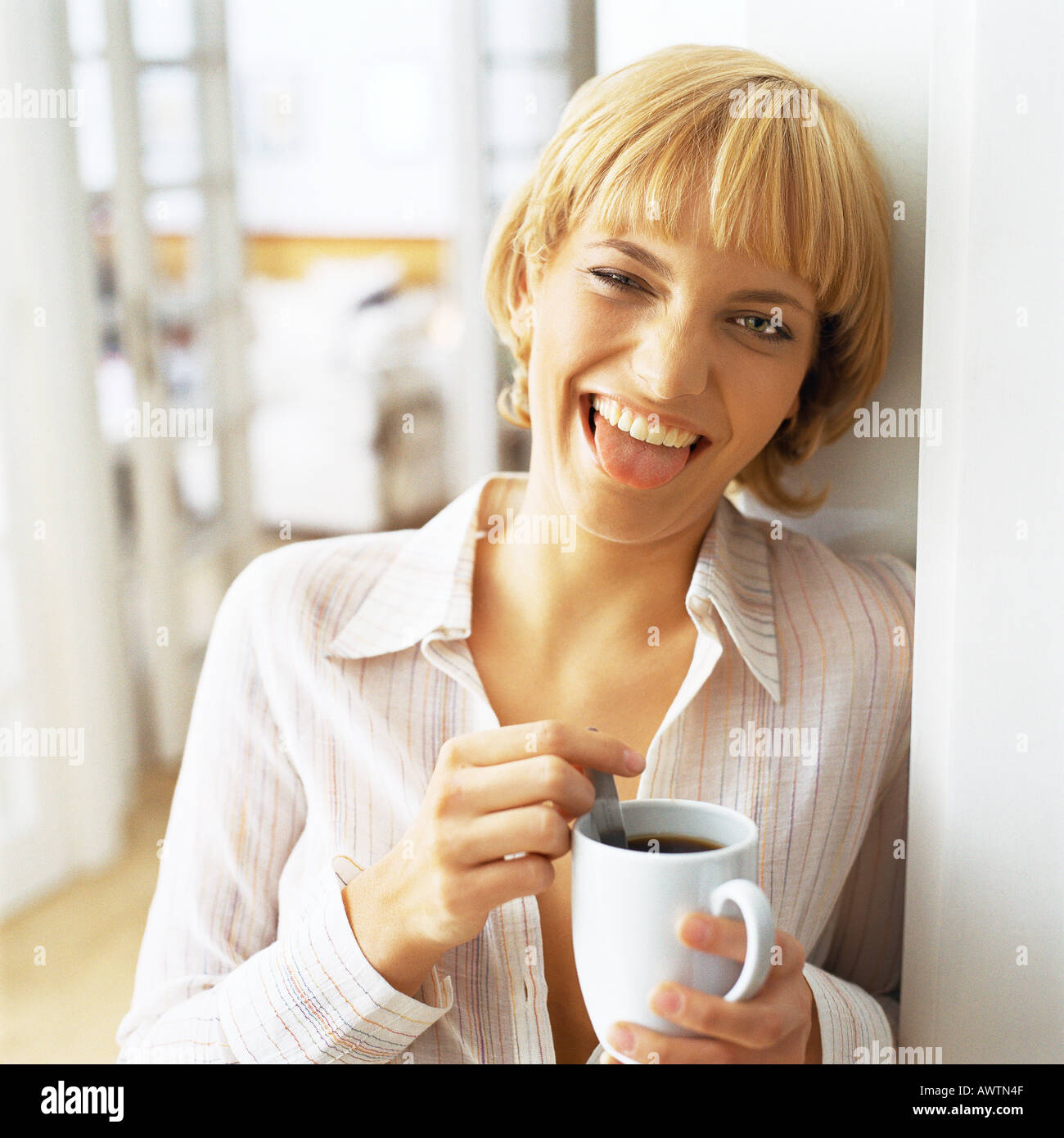 Teen girl holding tasse de café, sticking tongue out at camera Banque D'Images