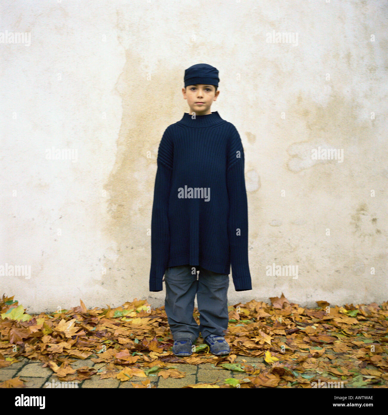 Garçon debout parmi les feuilles d'automne, le port de chandail surdimensionné Banque D'Images