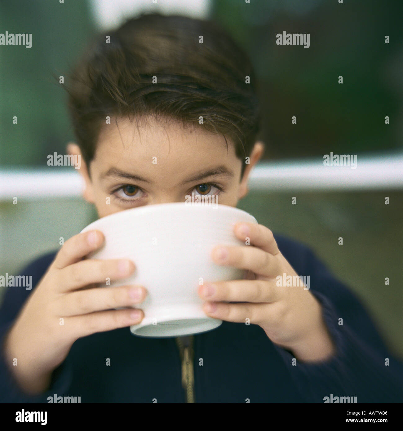 Boy drinking from bol, looking at camera sur le bord de la cuvette Banque D'Images