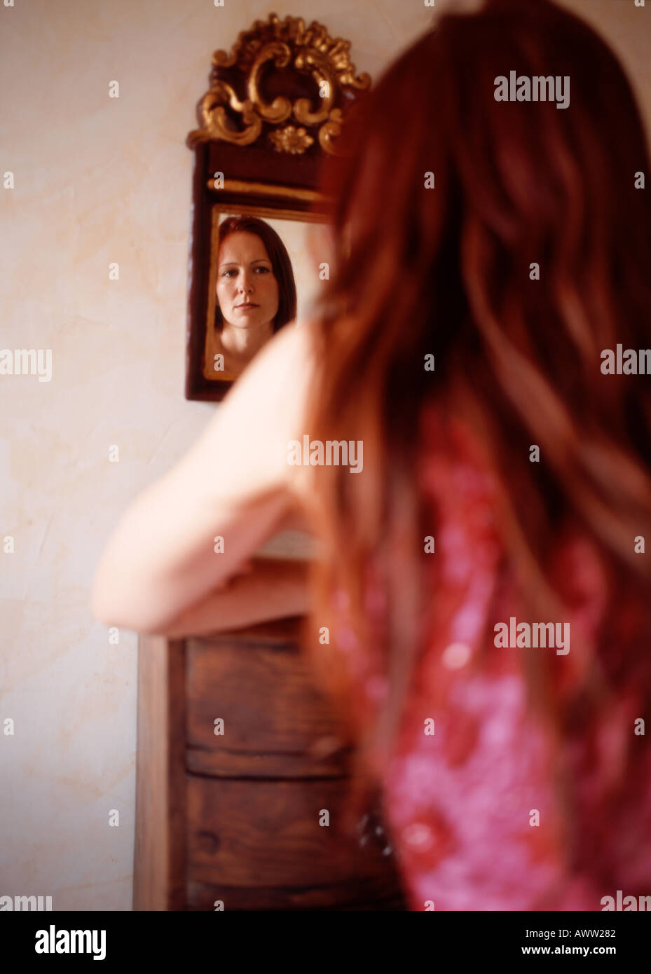 Red haired woman looking in mirror, vue arrière Banque D'Images