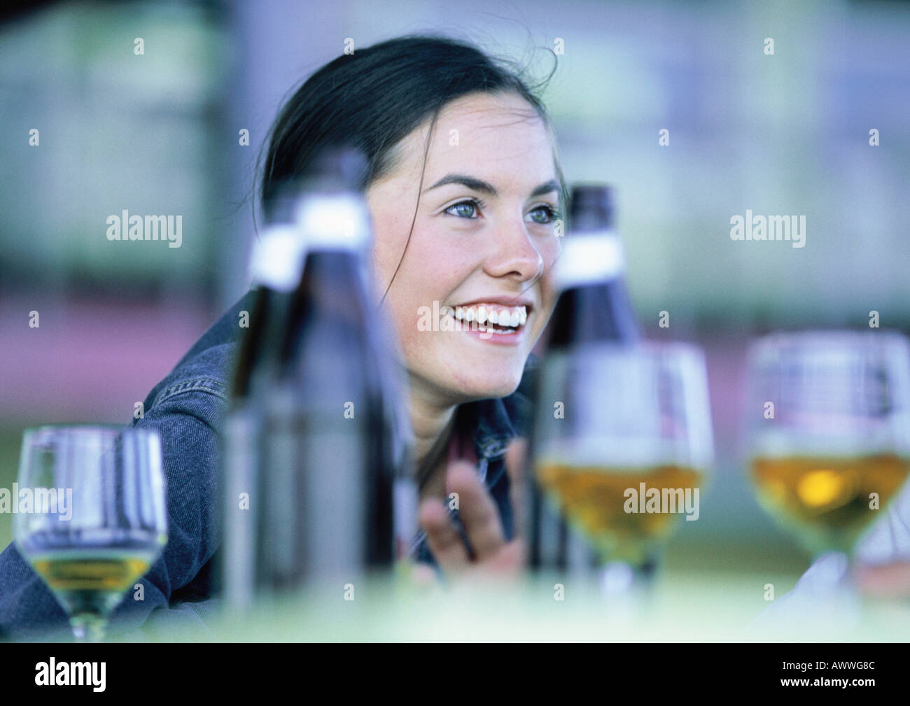 Teenage girl smiling à table avec bouteilles et verres Banque D'Images