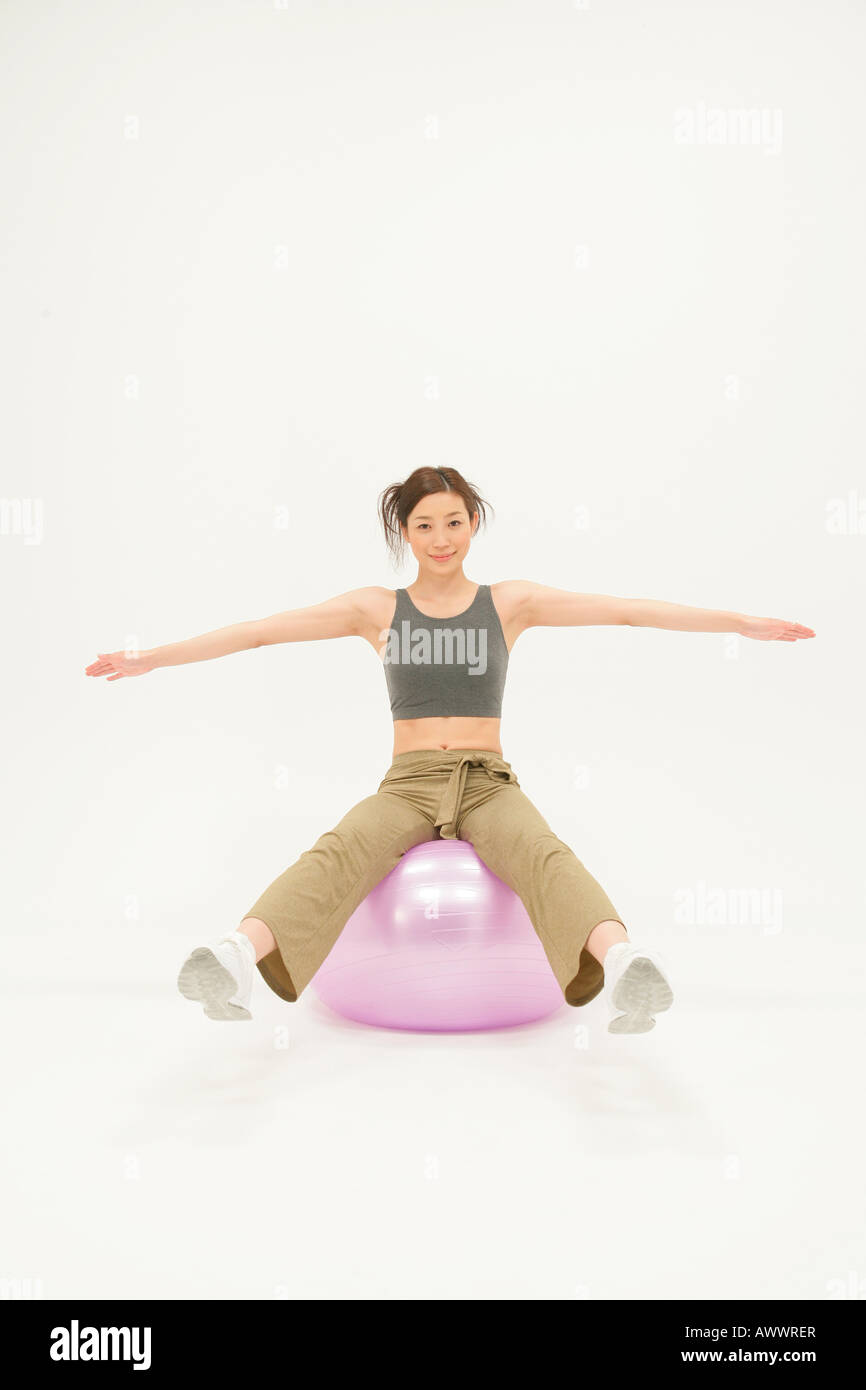 Studio portrait of young woman with arms outstretched on exercise ball Banque D'Images