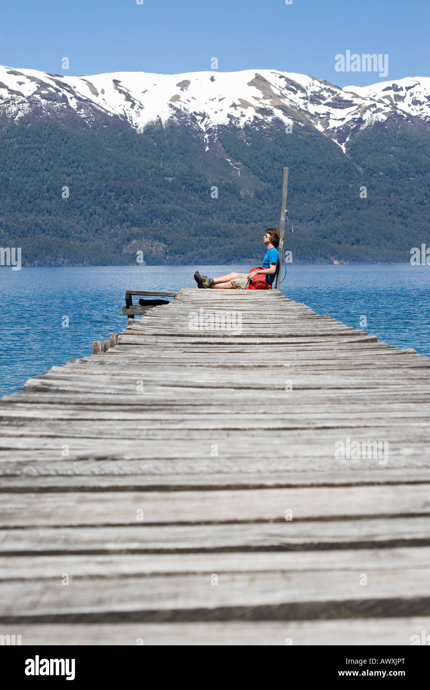 La Figure d'hommes assis sur fin de jetée du lac avec des montagnes enneigées en arrière-plan Banque D'Images