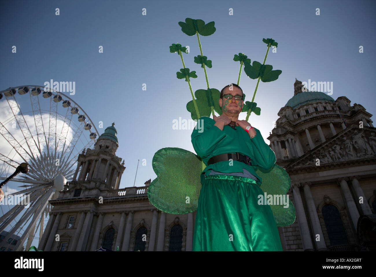Stiltwalker habillé en vert portant des trèfles à Belfast City Hall et grande roue avant la parade et le carnaval St Patricks day Banque D'Images