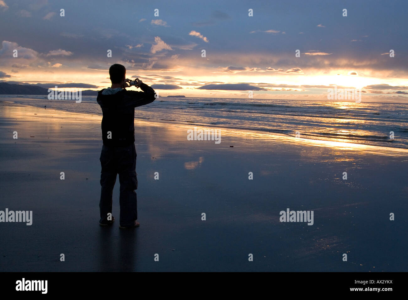 La Figure masculine Taking Photograph Silhouetté sur la plage au coucher du soleil Banque D'Images