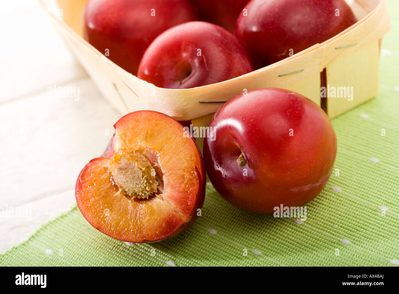 Close-up de prunes rouges en petit panier, ensemble et à l'avant, demi-toile verte sur la table Banque D'Images