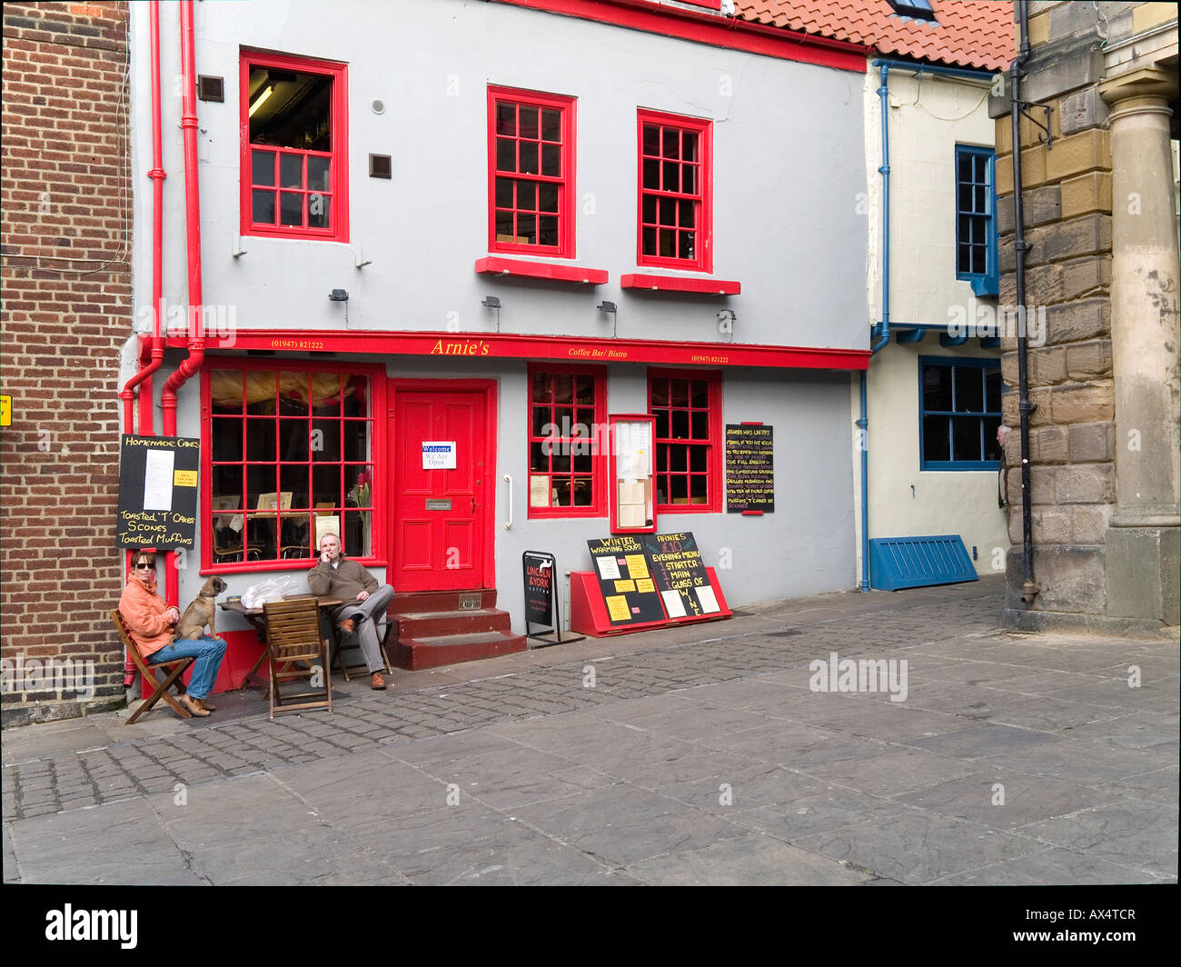 Homme et une femme avec un chien sur ses genoux assis à l'extérieur d'un café, à Whitby, North Yorkshire UK Banque D'Images