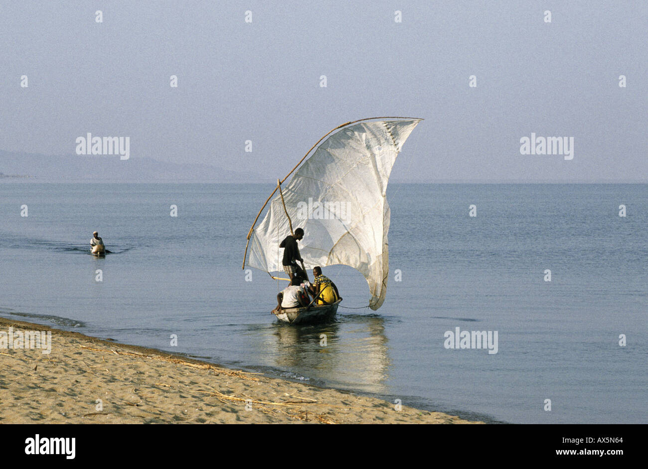 Le lac Tanganyika, en Tanzanie. Avec un boutre voile patchwork blanc d'être lancé comme un canot arrive. Banque D'Images