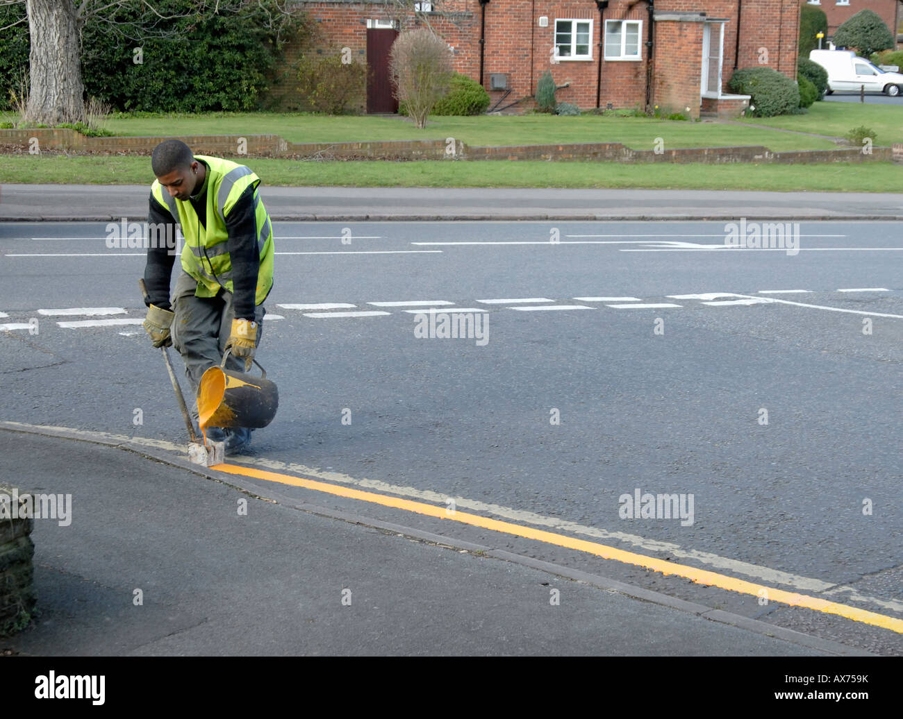 Jeune homme peinture ligne jaune sur road intersection avec électrique de peinture de marquage à chaud et de l'outil, Cheam, le sud de Londres, Surrey Banque D'Images