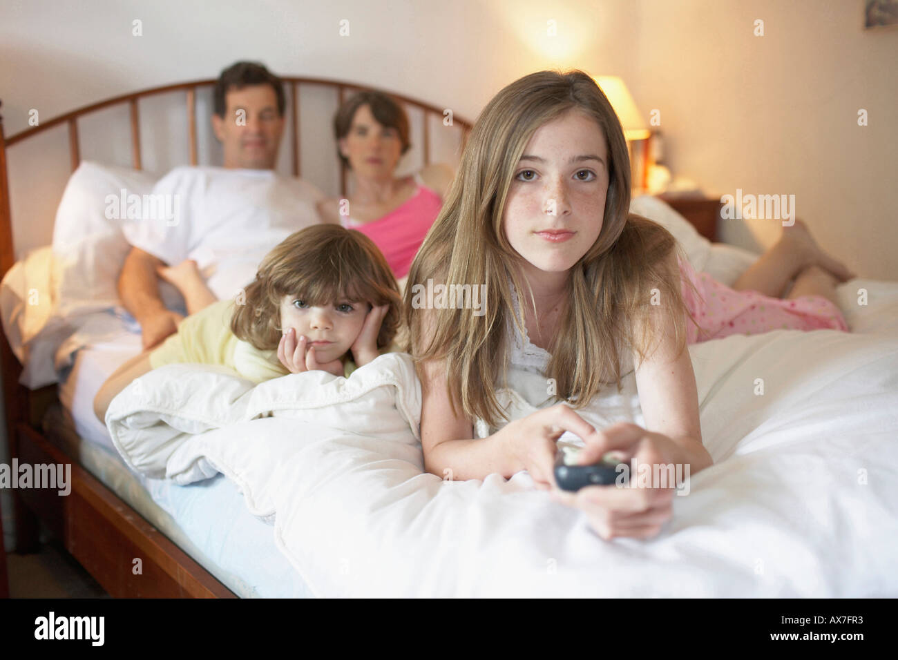 Adolescente et sa sœur avec leurs parents couché dans le lit en regardant la télé Photo Stock