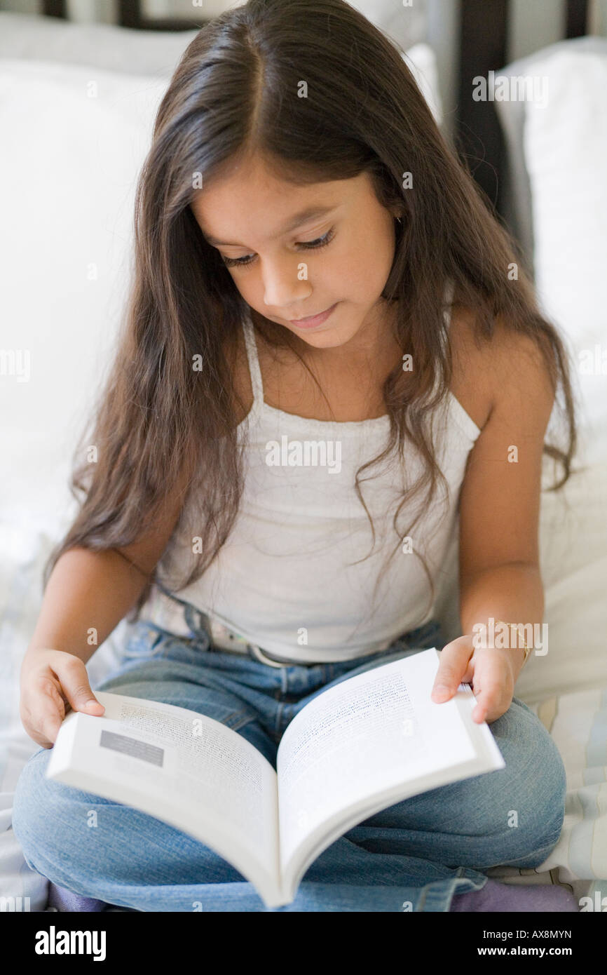 Jeune fille assise sur le lit en lisant un livre. Banque D'Images