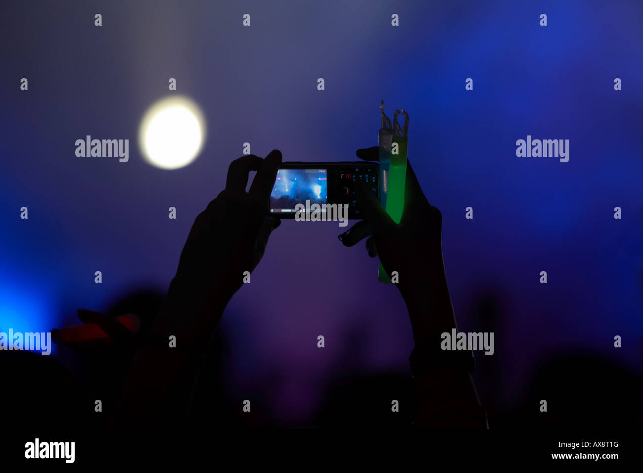 Mains en l'air dans la foule en tenant une vidéo avec un téléphone mobile et tenant un bâton lumineux à un événement de danse dans le Nord de Belfast Irel Banque D'Images