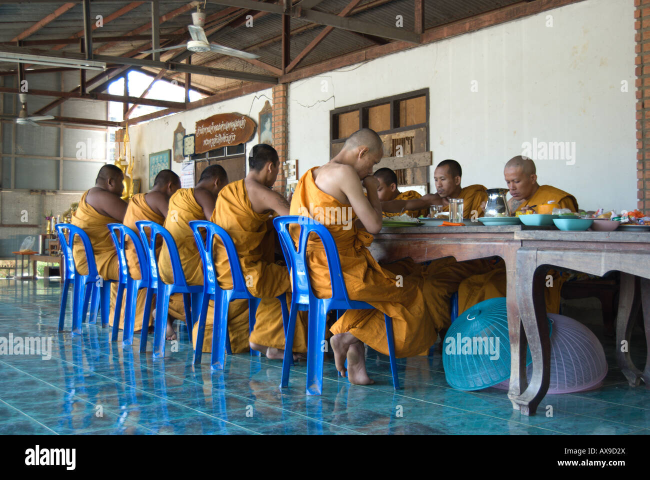 Assis sur des chaises en plastique bleu à une table, thai moines bouddhistes en robe jaune manger un délicieux repas dans un temple près de Phetchabun, Thaïlande Banque D'Images