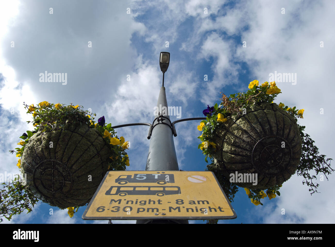 Deux paniers suspendus remplis de fleurs à un lampadaire, qui détient également un noir et jaune en signe de la circulation routière Banque D'Images