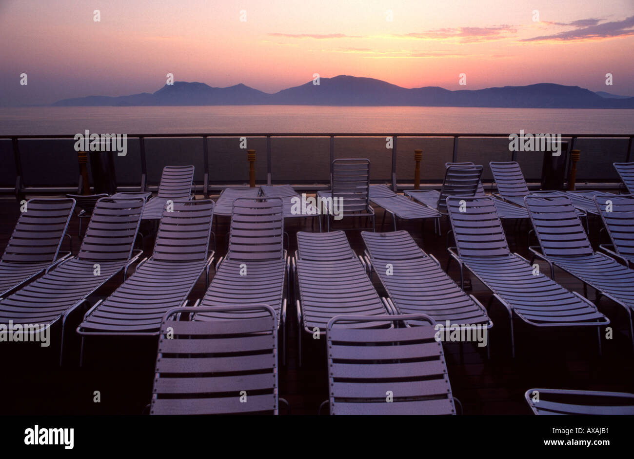 Pile de chaise longue en plastique vide de chaises sur un pont de passagers d'un navire de croisière au coucher du soleil Banque D'Images
