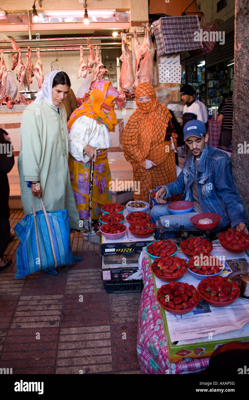 Marché d'Agadir, Maroc, Afrique du Nord-Ouest. L'homme en bleu la vente de fraises aux femmes. orange robe. Banque D'Images