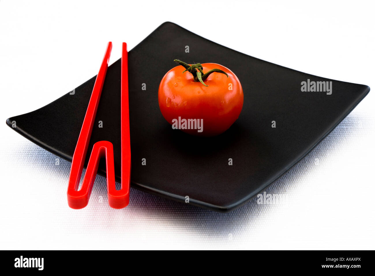 Une tomate rouge et rouge baguettes sur une plaque d'oriental noir carré Banque D'Images