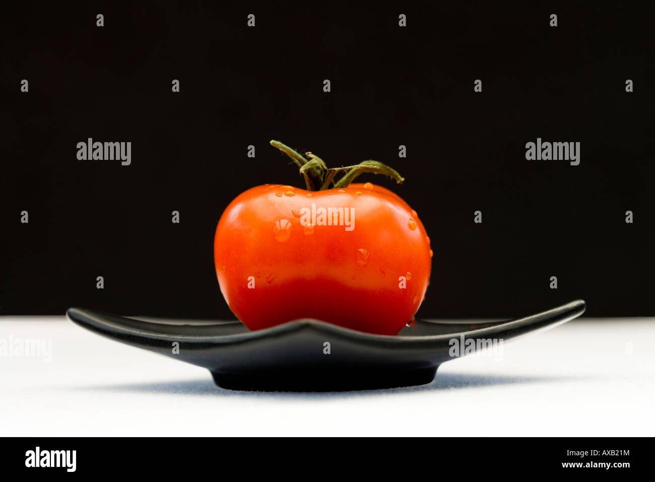 L'un rouge tomate sur une plaque d'oriental noir carré Banque D'Images