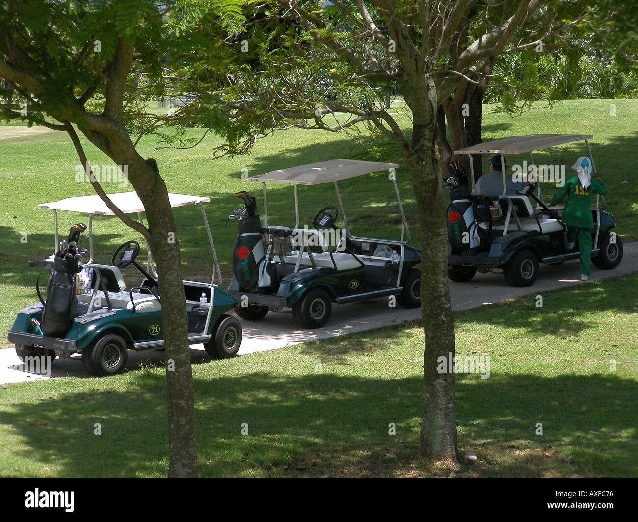 Des voiturettes de golf trois garée à l'ombre, femme caddie escalade en premier, Phoenix Golf and Country Club Pattaya Thaïlande Banque D'Images
