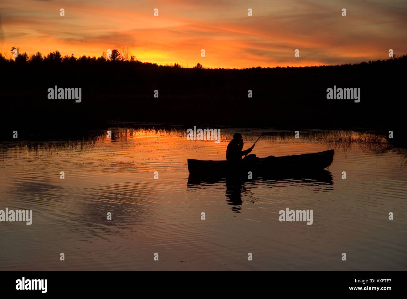 Un chasseur de canard est assis dans son canoë au coucher du soleil tandis que la chasse. Banque D'Images