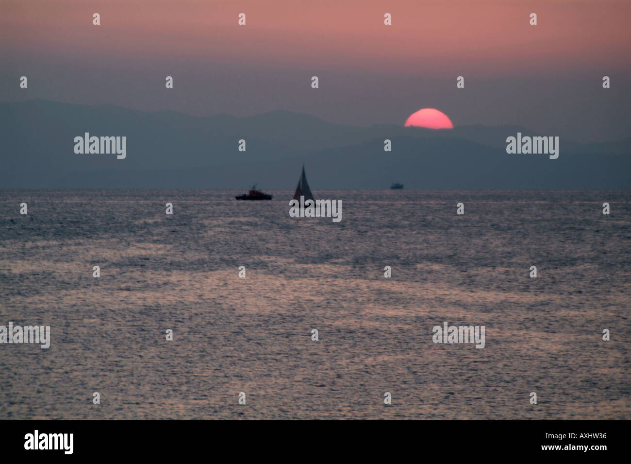 Vue sur les bateaux en mer avec le soleil rose en dessous de montagnes au loin en arrière-plan Athènes Banque D'Images