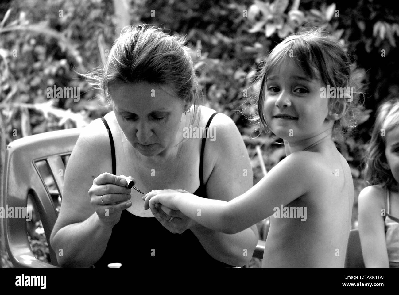 Jeune fille (4 ans) ayant ses ongles peints par sa mère. Noir et blanc, monochrome. Banque D'Images