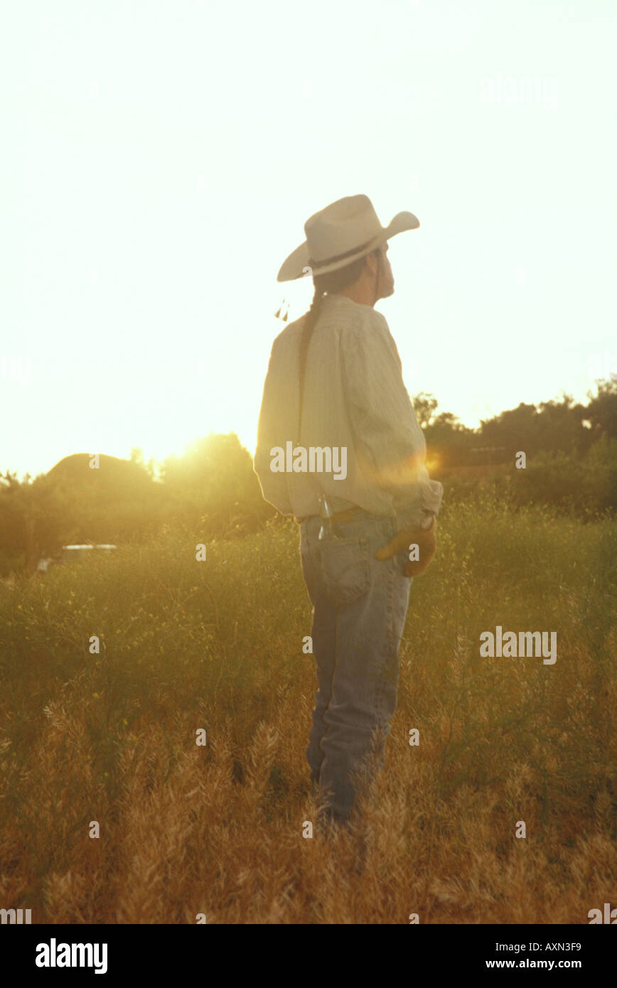 Un homme de race blanche adultes de l'ouest américain se tient dans un champ de cow-boy dans un ranch en contemplant le coucher du soleil à Santa Fe, Nouveau Mexique. Banque D'Images