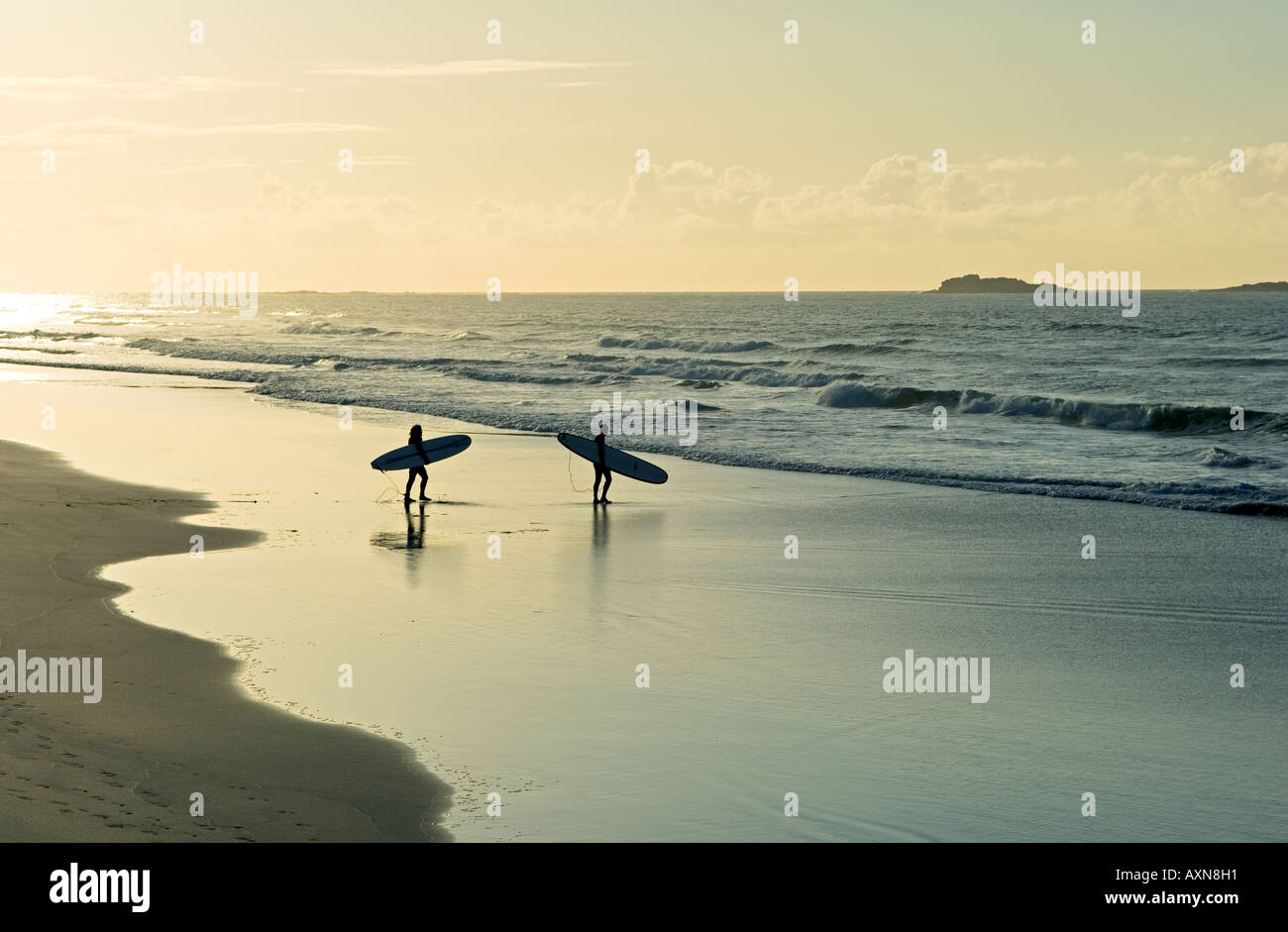 Surfeurs transportant des planches de surf marchant le long de la plage de sable fin le soir de l'été léger. White Rocks Strand, Portrush, Irlande Banque D'Images