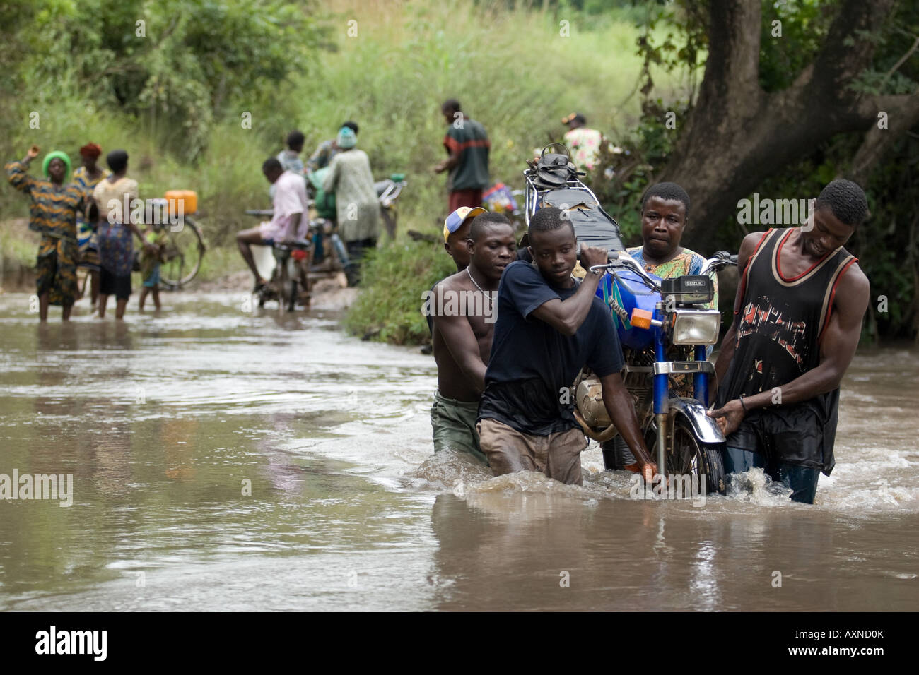 Un groupe d'hommes transporter une moto à travers une rivière Overflowing Banque D'Images