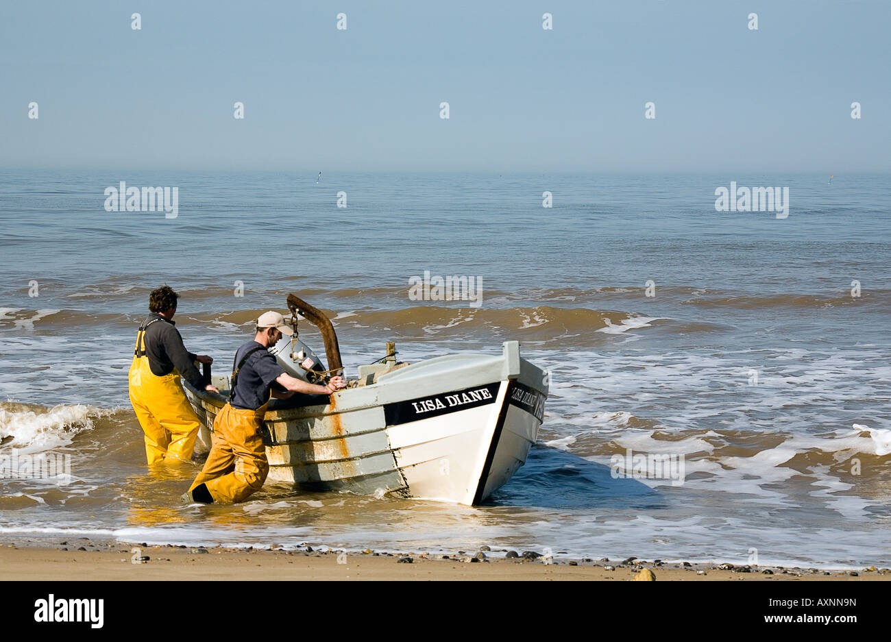 Deux pêcheurs apportant leur bateau et s'accrochent à plage de Cromer, Norfolk. Banque D'Images