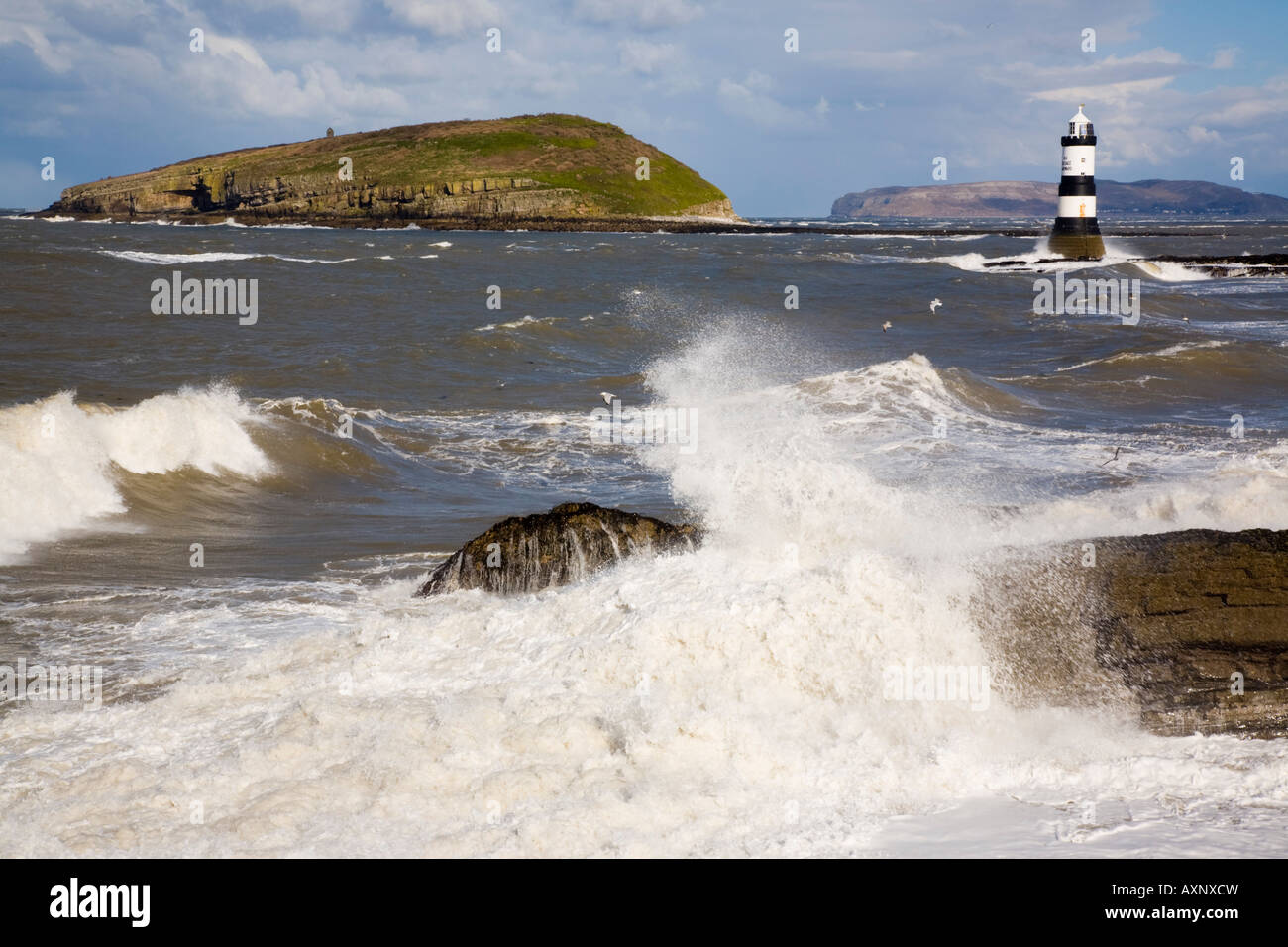 Penmon Point Anglesey au nord du Pays de Galles UK mer houleuse tempête de vent Penmon leuchtturm de grosses vagues en avant-plan sur la côte rocheuse Banque D'Images