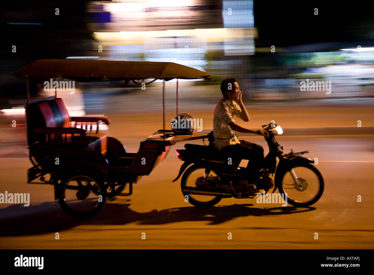 Des vitesses par un conducteur de pousse-pousse dans la nuit tout en discutant sur un téléphone cellulaire - un signe que le Cambodge est en train de moderniser Banque D'Images