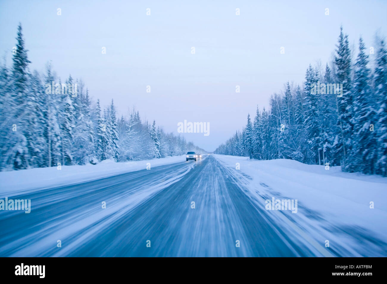 Drivers voir d'aborder la circulation sur route couverte de neige avec effet de mouvement flou lever du soleil d'hiver de l'autoroute de l'Alaska États-unis Parcs Banque D'Images
