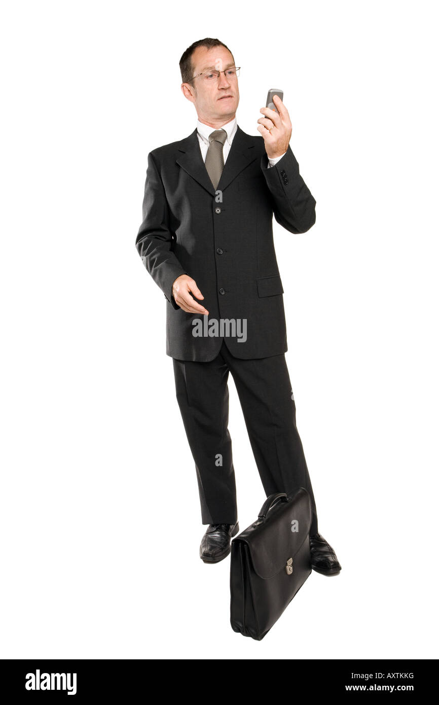 Homme d'affaires debout dans un costume noir regarde son téléphone portable qu'il a dans sa main. Le fond est blanc pur. Banque D'Images