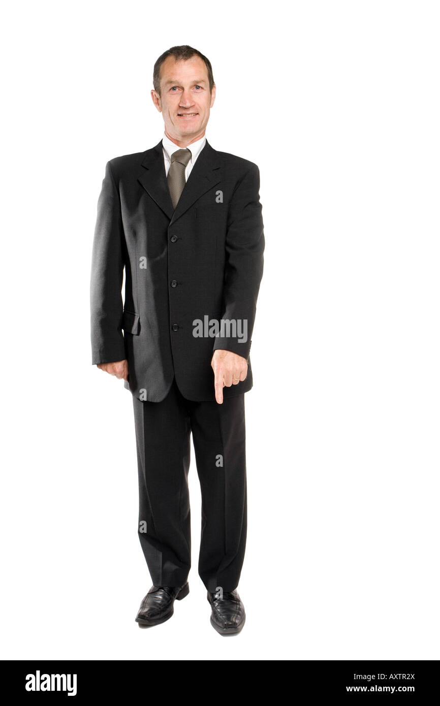 Homme d'affaires debout dans un costume noir montrant la direction du bas sur le sol avec son doigt. Le fond est blanc pur. Banque D'Images