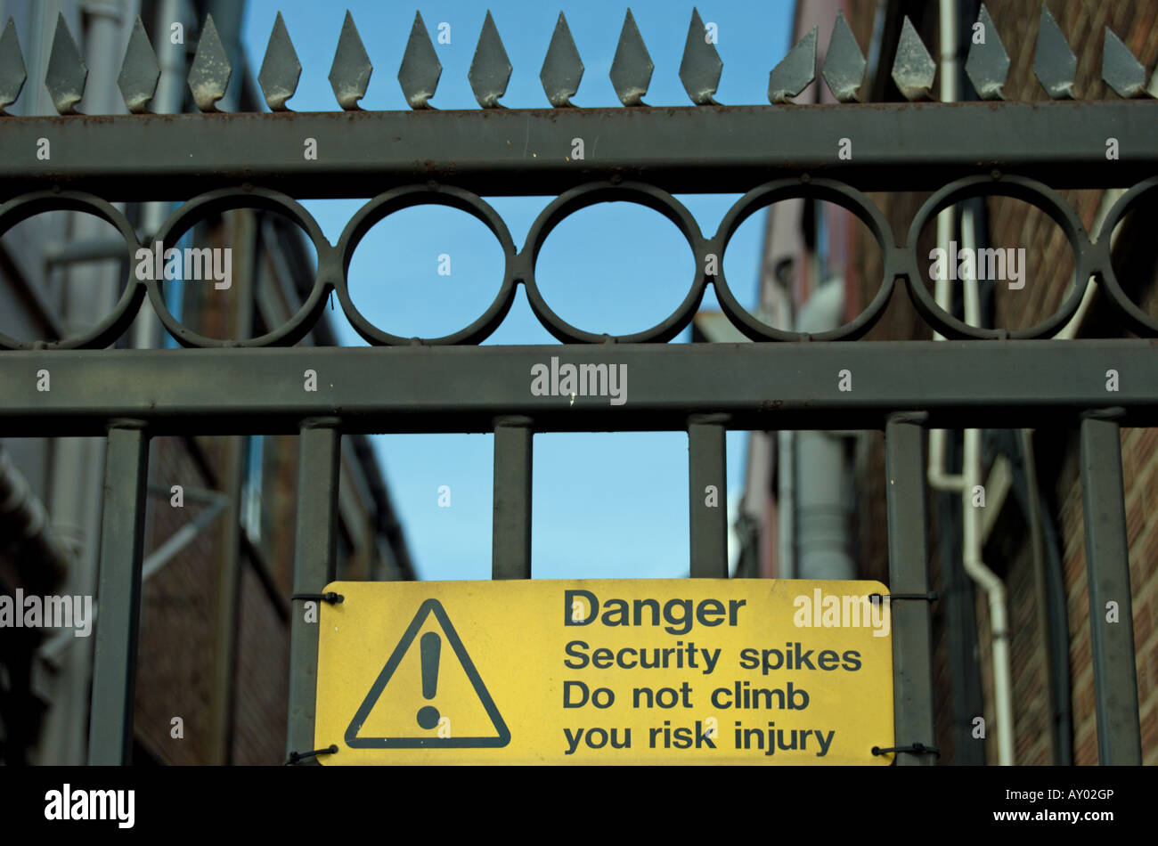 Panneau jaune avec la zone de texte met en garde contre les pointes de sécurité en haut d'une clôture, situé sur la North Circular Road, Londres, Angleterre Banque D'Images