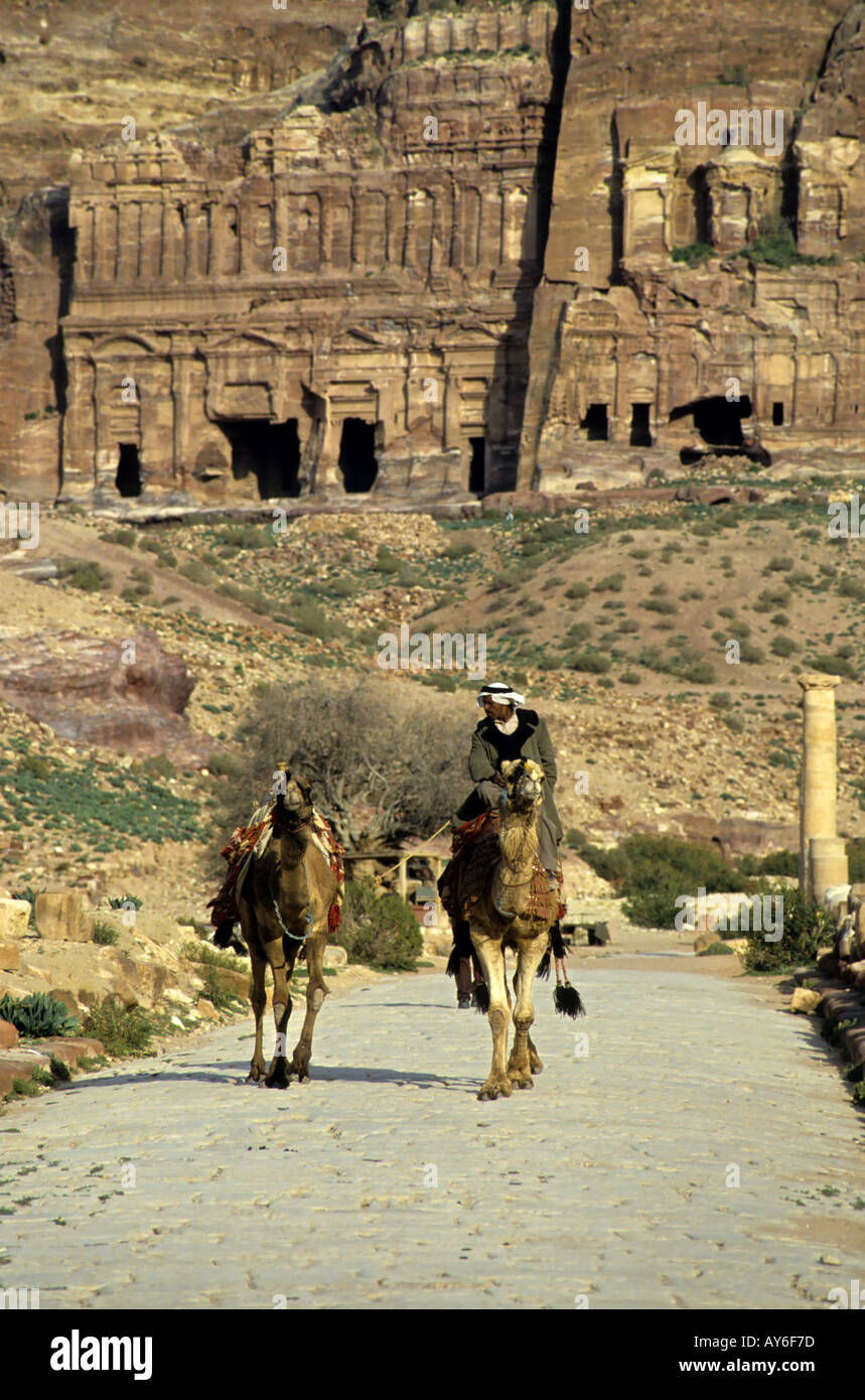L'homme monté sur un chameau sur une route pavée, près de l'entrée du Royal Tombs creusé dans les falaises à Pétra, en Jordanie. Banque D'Images