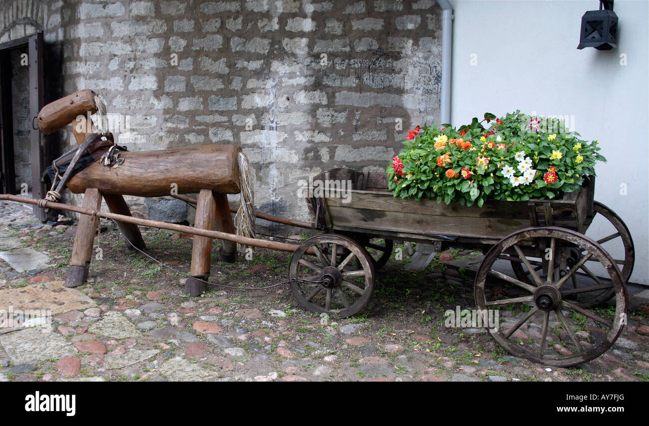 Cheval de bois décorative tirant un vieux wagon en bois remplis de fleurs, en face du vieux bâtiment en brique de cour en pierre blanche Banque D'Images