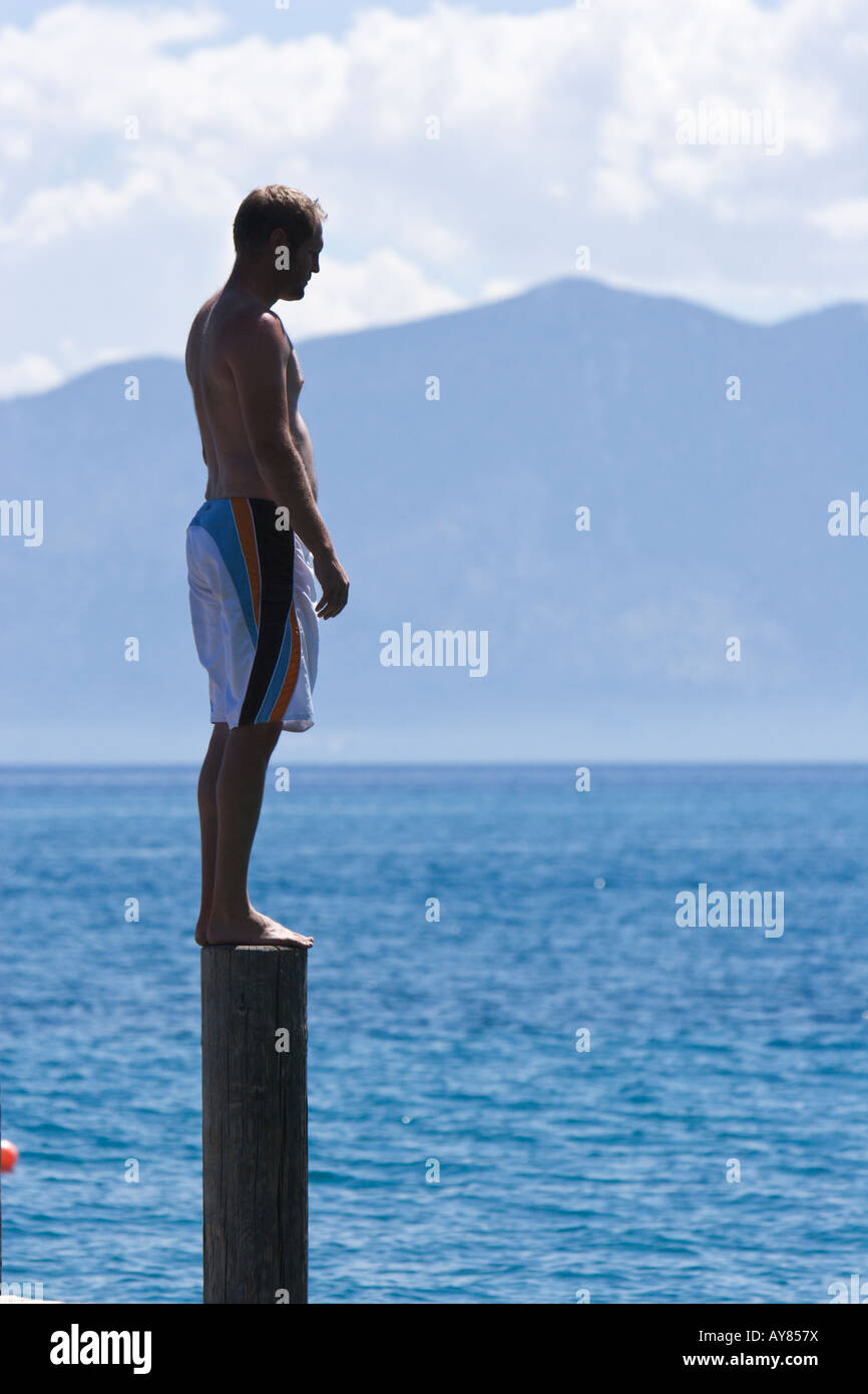 Profil d'un homme debout sur le post en bois avec bras tendus avec montagnes, lac, et les nuages en arrière-plan. Banque D'Images