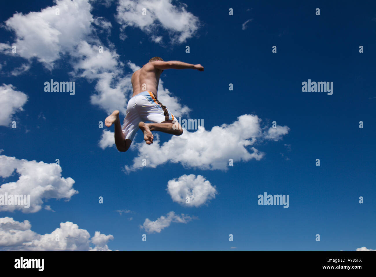 Un homme en maillot saute en l'air les bras en l'air et les jambes à coups de retour avec un ciel bleu et nuages dans l'arrière-plan. Banque D'Images