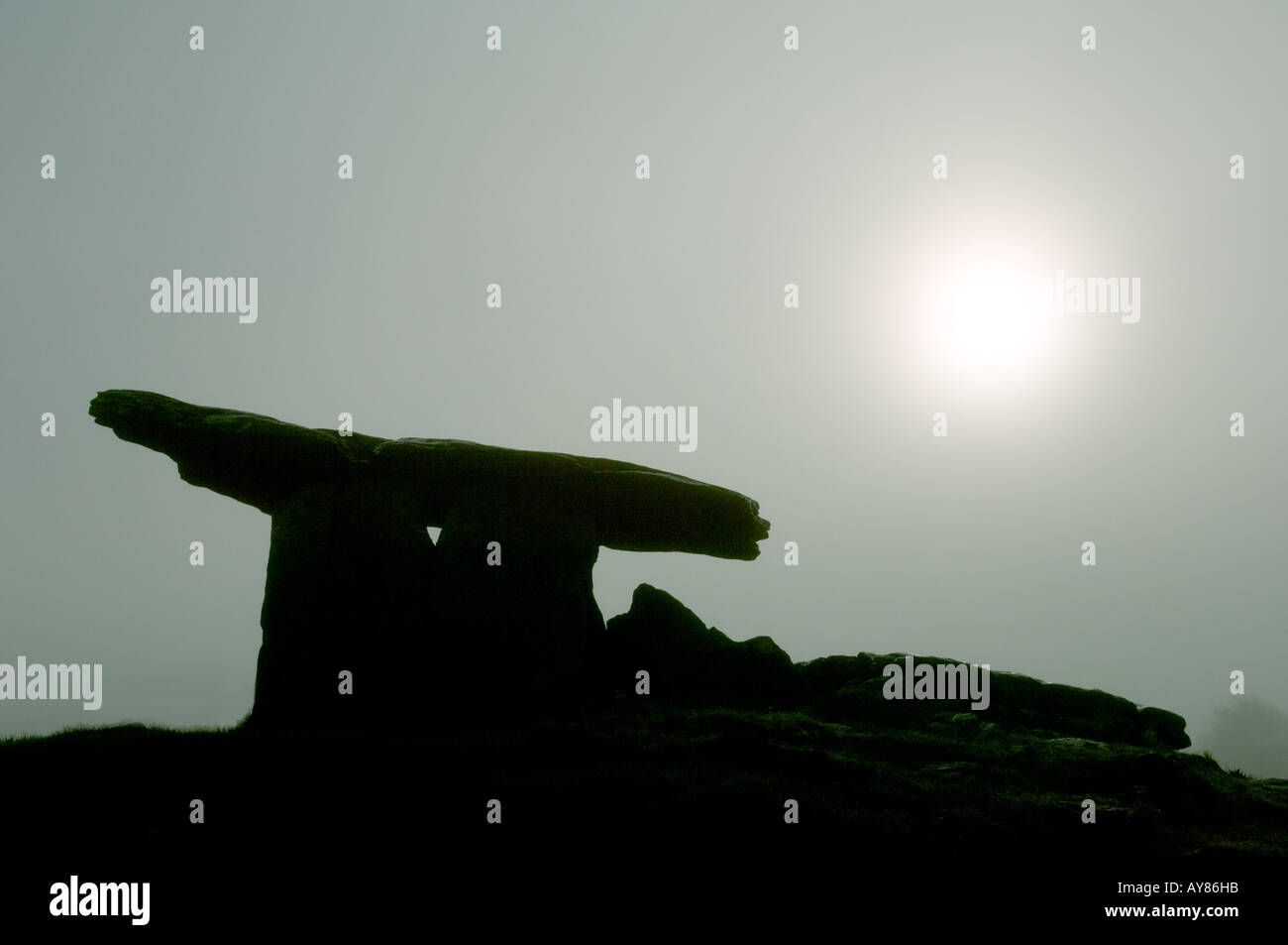 Dolmen de Poulnabrone tombeau préhistorique silhouetté contre lune soleil dans la brume sur le plateau calcaire du Burren, comté de Clare, Irlande. Banque D'Images