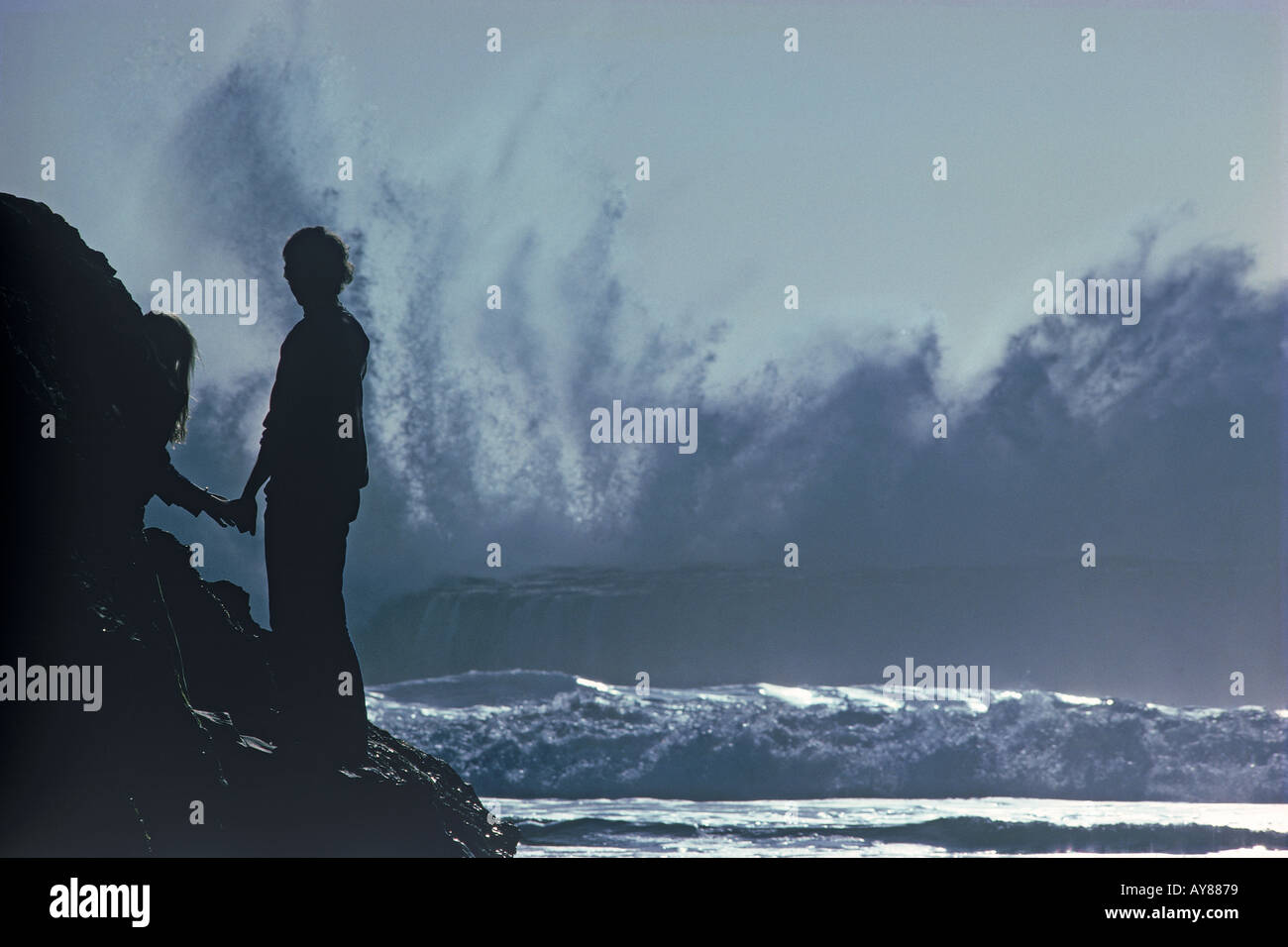 Les ondes de tempête battant Big Sur rocky shore avec couple watching Banque D'Images