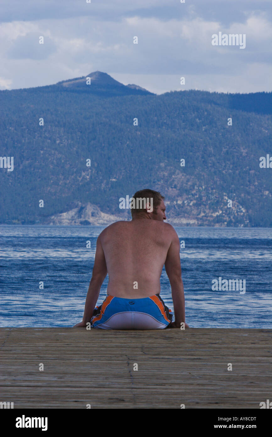 Un homme est assis sur le bord d'un lac Tahoe pier avec montagnes en arrière-plan. Banque D'Images