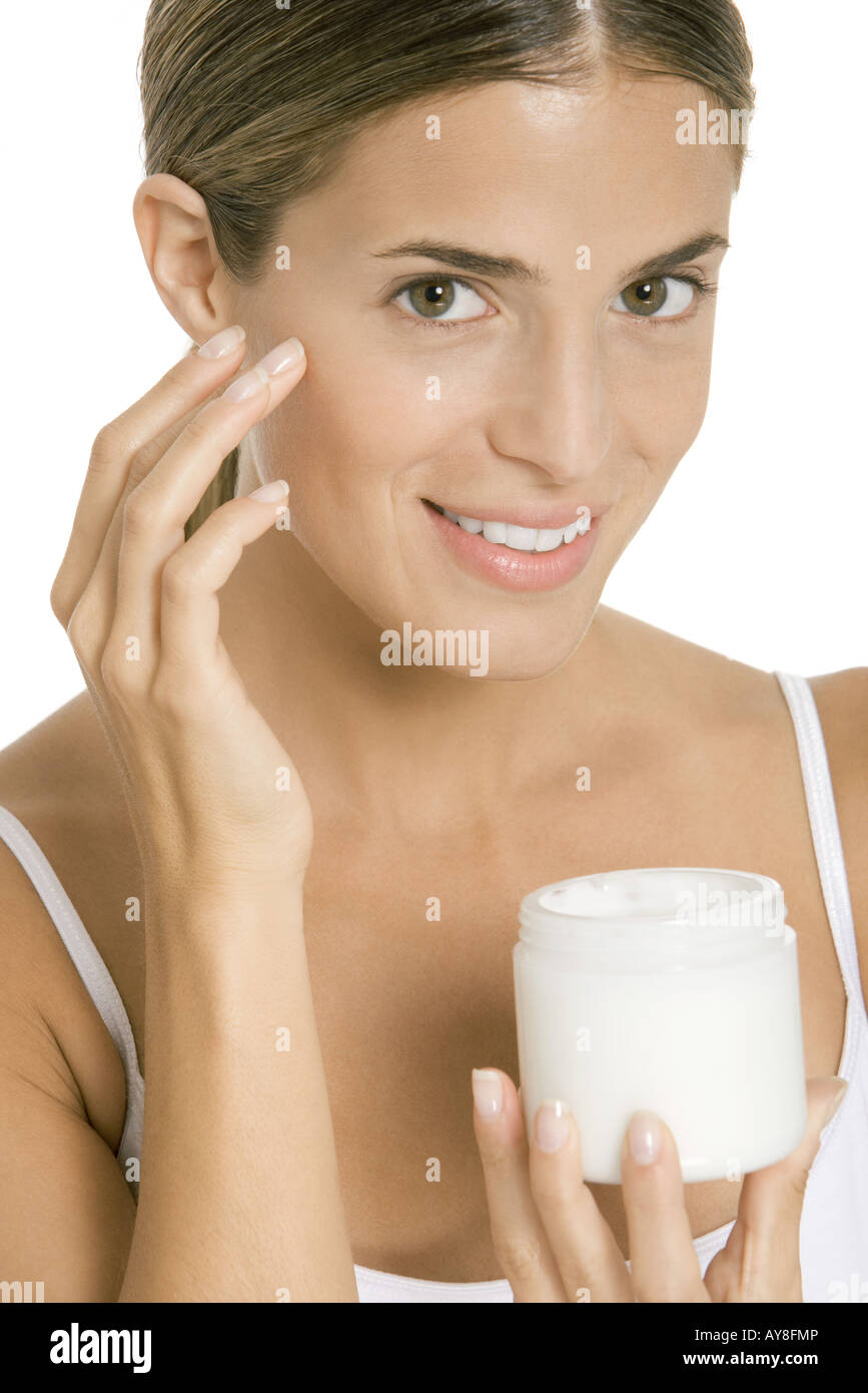 Woman applying moisturizer to face, smiling at camera Banque D'Images