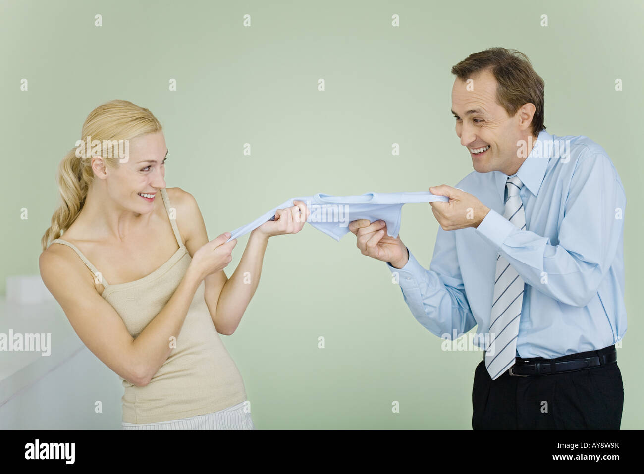 Couple fighting over baby clothing, smiling at each other Banque D'Images