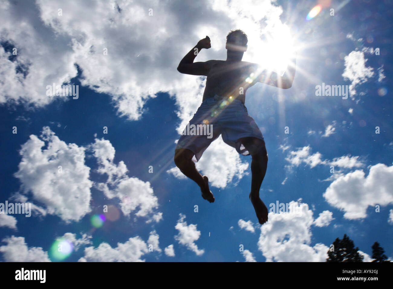 Un homme en maillot saute en l'air les bras en l'air et les jambes à coups de retour avec un ciel bleu et nuages dans l'arrière-plan. Banque D'Images
