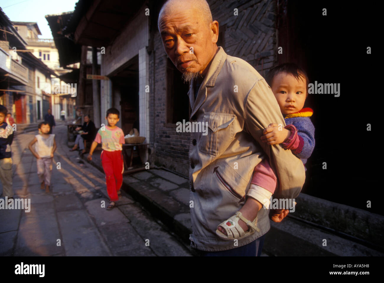 La province du Sichuan en Chine Shi Bao Zhai vieil homme porte bébé à travers des rues du village le long du fleuve Yangtze Banque D'Images